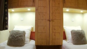 Ein Zimmer mit zwei Betten, jeweils mit einer weißen Matratze und einem grauen, flauschigen Kissen. Das Zimmer verfügt über Holzschränke mit einer zentralen Tür und eingelassene Beleuchtung an der Decke.