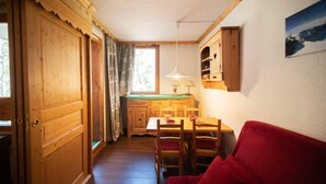 Un interior de madera con una mesa de comedor, sillas, un sofá rojo y una zona de cocina con armarios de madera y una ventana.