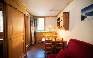 Un interior de madera con una mesa de comedor, sillas, un sofá rojo y una zona de cocina con armarios de madera y una ventana.