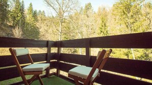 Una terraza de madera con dos sillas y una mesa, con vistas a una zona boscosa.
