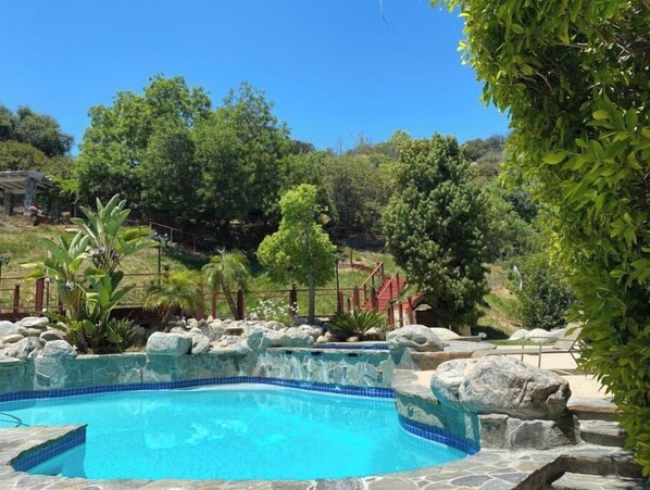 Relax by the serene pool surrounded by lush greenery and a natural stone border.