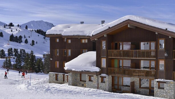 Eine mehrstöckige Lodge mit Stein Fundamenten und Holz Balkonen, eingebettet in eine verschneite Berglandschaft.