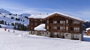 Eine Holzhütte mit Steinunterbau, mehreren Balkonen und einem mit Schnee bedeckten Dach, gelegen an einem verschneiten Berghang.