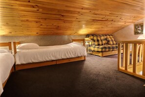 A room with a wooden ceiling, a bed with white bedding, a sofa with a checkered blanket, and a small wooden table.