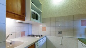 Een kleine keuken met een spoelbak, fornuis, magnetron en vaatwasser.