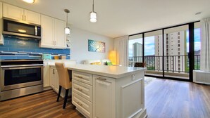 Una cocina moderna con electrodomésticos de acero inoxidable, una isla grande y vistas a un paisaje urbano desde el balcón.