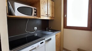 A compact kitchen with a microwave, stove, and dishwasher. There is a window providing natural light and a small trash bin. - 75m from shops, 2nd floor, view valley, balcony, ski locker, 27m², Méribel-Mottaret (Méribel - Les Allues)