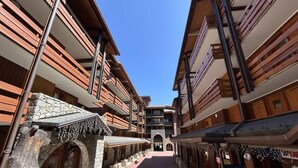 A corridor with wooden buildings, stone archways, and a clear blue sky. - 75m from shops, 2nd floor, view valley, balcony, ski locker, 27m², Méribel-Mottaret (Méribel - Les Allues)