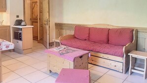 Um quarto acolhedor com um sofá de madeira, uma pequena mesa com toalha quadriculada e um espaço com cozinha compacta.