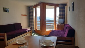 A room with a wooden table set for dining, a purple sofa, and a view through a glass door to the outside. - Wifi, 100m from ski slopes, 2nd floor, balcony, tv, ski locker, 27m², La Rosière (La Rosière Montvalezan)