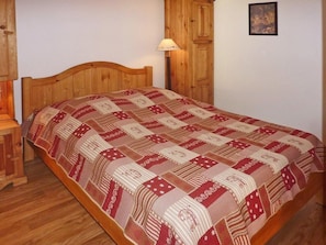A wooden bed with a patterned bedspread in a room with a wooden wardrobe and a nightstand.