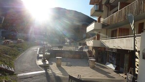 A commercial building with a balcony, a paved area with benches, and a mountain in the background.