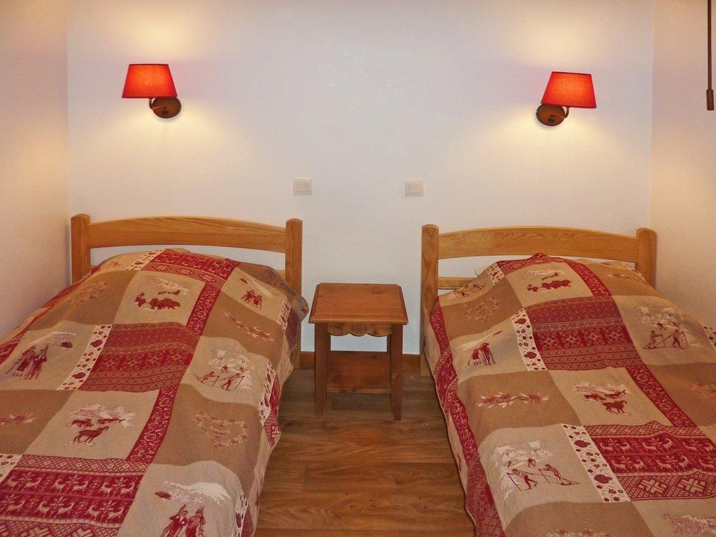 A room with two single beds, each with a wooden headboard, a small wooden nightstand, and a red wall lamp.