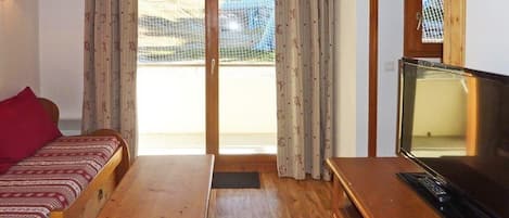 A room with a wooden bed, a wooden table, a television, and a view of a netted area outside.