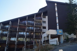 A multi-story building with balconies, a sign indicating a spa, and a stone structure nearby. - 3rd floor, tv, 25m², Sauze - Super Sauze (Enchastrayes)