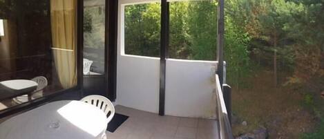 Un balcon donnant sur un paysage verdoyant, une table blanche et une chaise.