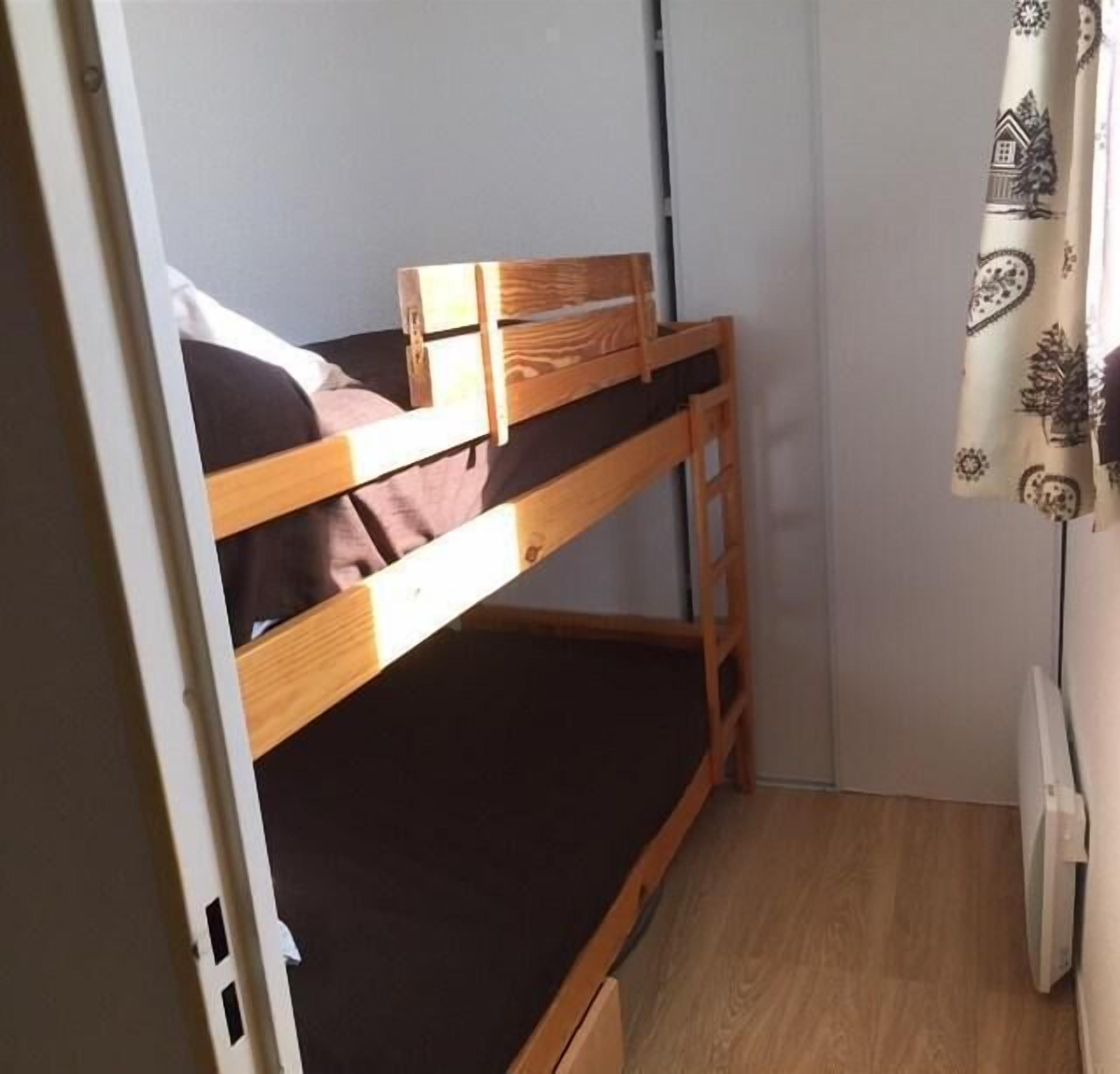 A bunk bed in a small room with a white wall and a window with curtains.