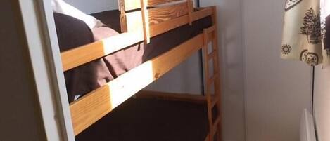 A bunk bed in a small room with a white wall and a window with curtains.