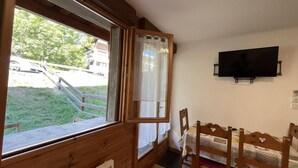 A small room with a wooden floor, a window with curtains, a bed with a white bedspread, a wooden chair, and a television on the wall. - Ground floor, terrace, tv, 40m², Pra Loup (Pra Loup)