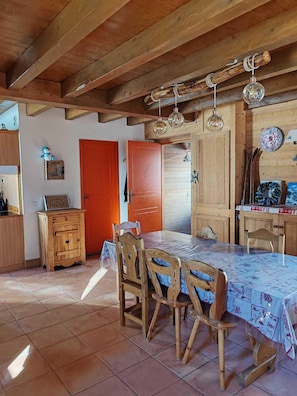 A rustic dining area with wooden furniture, a tiled floor, and a wooden ceiling with exposed beams.