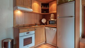 A compact kitchen with wooden cabinets, a built-in oven, a dishwasher, a microwave, and a refrigerator.