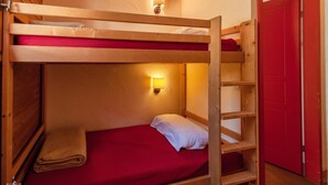 A bunk bed with a red mattress, a white pillow, and a wall-mounted light fixture.