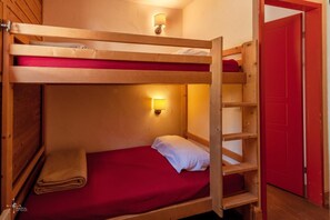 Una cama litera con colchón rojo, almohada blanca y lámpara fijada a la pared.