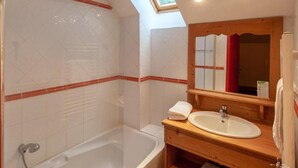 A bathroom with a skylight, a bathtub, a sink, and a wooden vanity.