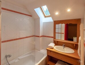 Un baño con tragaluz, bañera, lavamanos y tocador de madera.