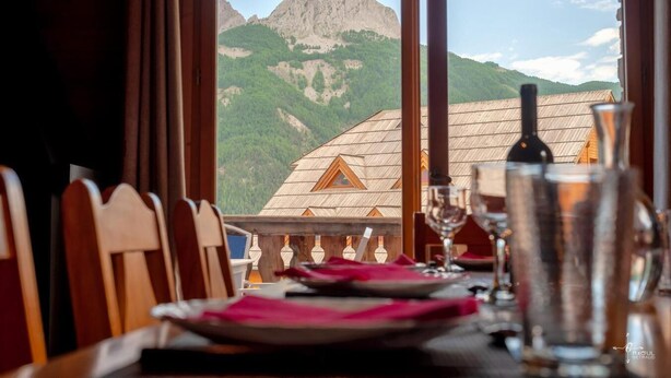 A dining table set for two with a mountain view through large windows.