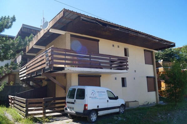 Ein zweistöckiges Gebäude mit einem hölzernen Balkon und einem weißen Lieferwagen davor.