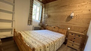 A bedroom with a wooden bed, a bedside table, a wardrobe, and a window with curtains.