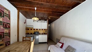 A compact living space with a wooden dining table, a sofa, and a kitchen area with a tiled backsplash.