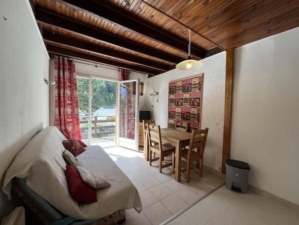 Un dormitorio con cama, una mesita y sillas, una ventana con cortinas, y vistas al exterior.