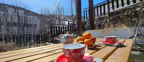 A wooden table with a teapot, cups, and oranges.