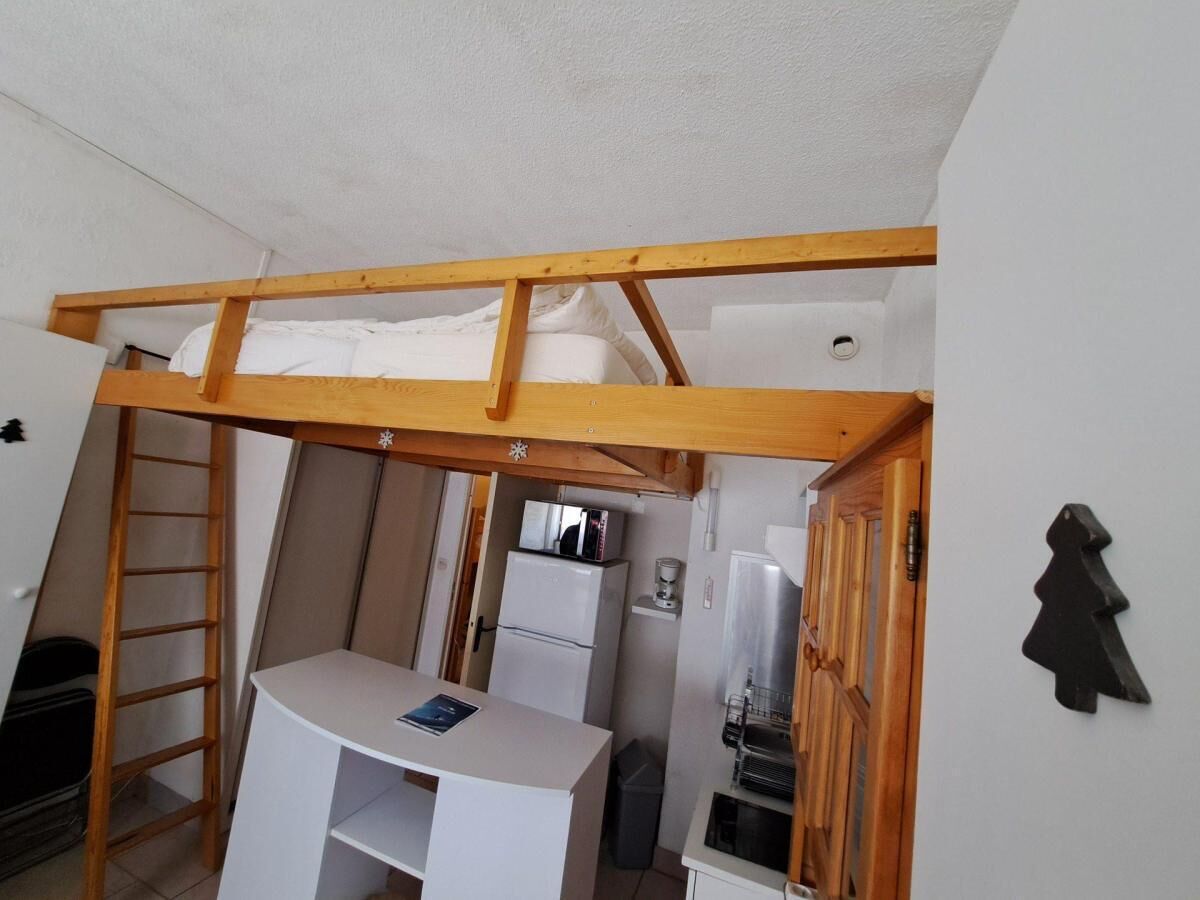 Una habitación pequeña con cama tipo litera, un escritorio y un refrigerador.