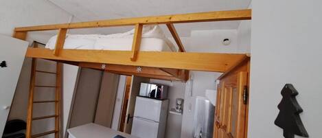 Una habitación pequeña con cama tipo litera, un escritorio y un refrigerador.
