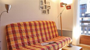 A cozy room with a plaid sofa, a small wooden table, and a floor lamp. - 50m from ski slopes, 5th floor, balcony, tv, ski locker, 23m², Risoul (Risoul)