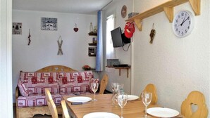 A dining area with a wooden table set for two, a patterned sofa, and a wall clock. - 100m from ski slopes, 1st floor, balcony, tv, ski locker, 28m², Risoul (Risoul)