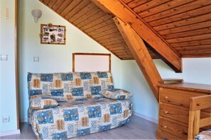 A cozy attic bedroom with a wooden ceiling, a patterned sofa, and a wooden dresser. - 10m from resort center, 6th floor, view ski slopes, swimming pool, balcony, tv, ski locker, 31m² (Risoul)