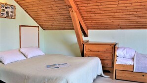 Une chambre avec un plafond en bois incliné, un lit, une table de chevet et une commode.