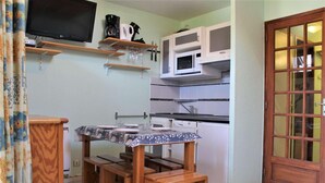 Une cuisine compacte comprenant une table à manger, des tabourets en bois, un four à micro-ondes et un téléviseur fixé au mur.