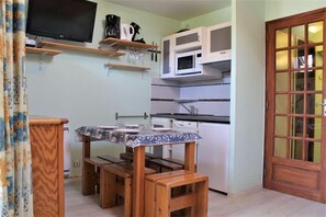 A compact kitchen with a dining table, wooden stools, a microwave, and a TV mounted on the wall. - 10m from resort center, 6th floor, view ski slopes, swimming pool, balcony, tv, ski locker, 31m² (Risoul)