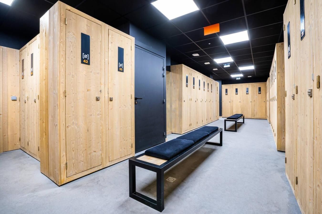 Une rangée de casiers en bois, chacun portant un numéro, un banc et une porte également numérotée.