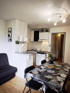 A compact kitchen with white cabinets, a black countertop, and a dining area with a table and chairs.