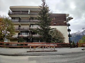 Un edificio a più piani con balconi, una recinzione in legno e una panchina di fronte.