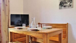 Una mesa de madera para comer con una televisión, un florero y vasos.