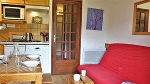 Un espacio habitable compacto con zona de comedor, un sofá rojo y una mesita con una revista.