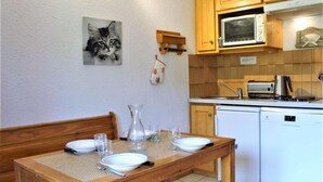Una mesa de comedor con platos, vasos y una jarrón, ubicada en una cocina con armarios de madera, un microondas y un lavavajillas.