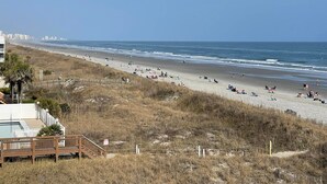 A beach with a wooden walkway leading to a building with a pool. - Inviting and Relaxing Beach and Golf Condo (North Myrtle Beach)